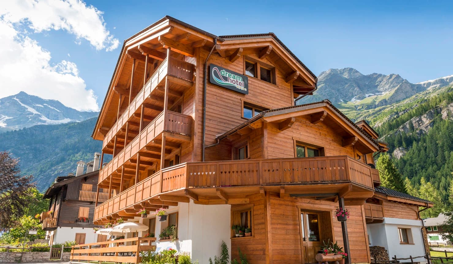 L’hotel di montagna di cui parla questa storia, visto dall’esterno in estate: un edificio in legno con i balconi fioriti, le cime delle Alpi alle spalle.